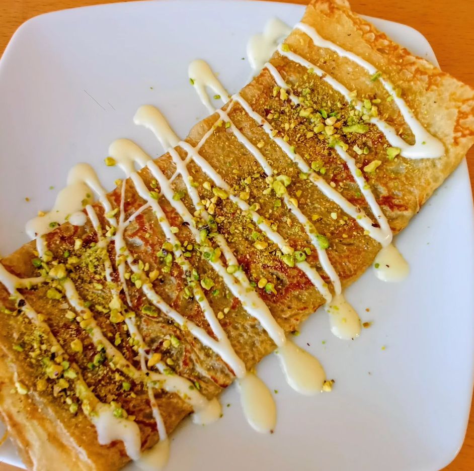 Crepe en plato blanco con salsa blanca y pistacho picado